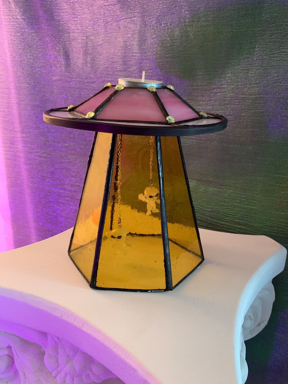 stained glass ufo with beam and two plastic aliens hanging inside with chains. the tea light goes on top