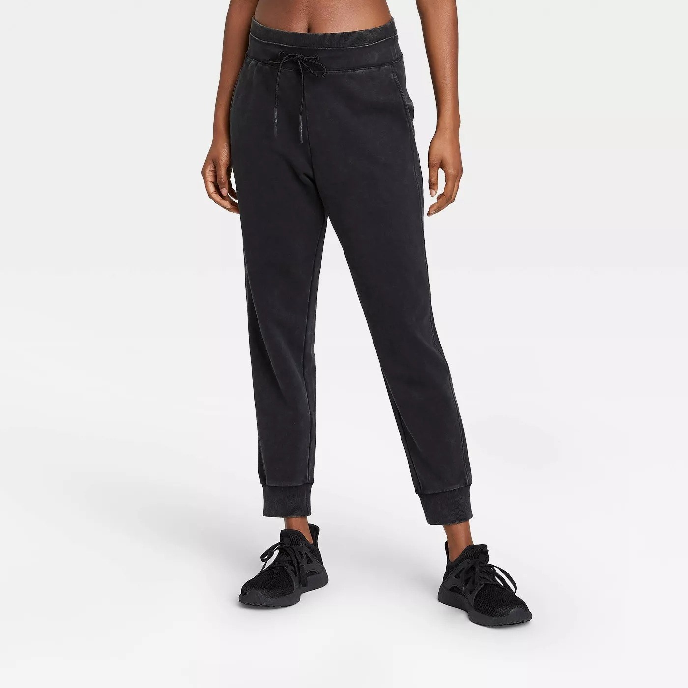 Model wearing black sweats cuffed at the bottom of the pants, stops at the ankle