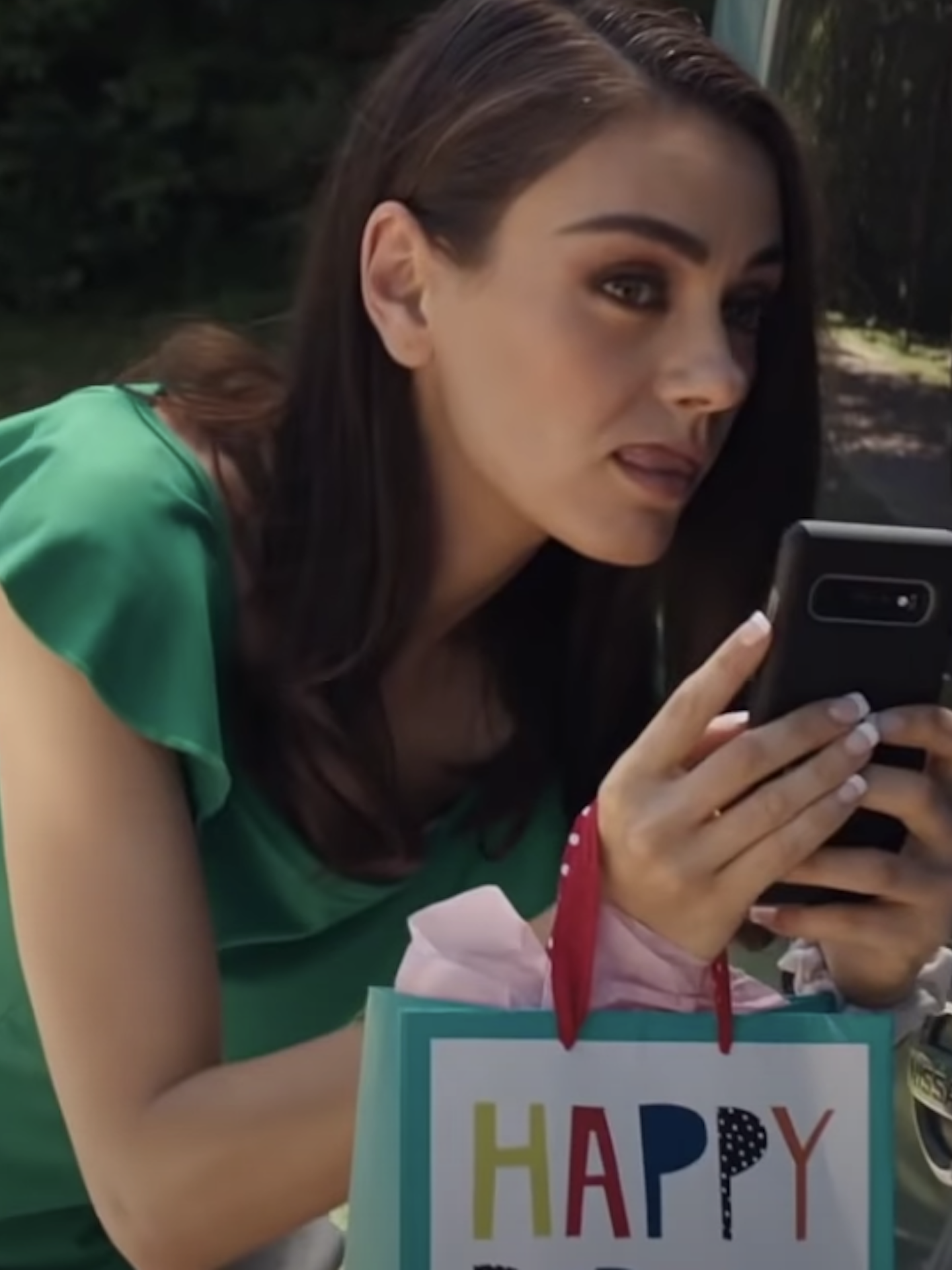 Mila Kunis holding an iPhone, spying on someone