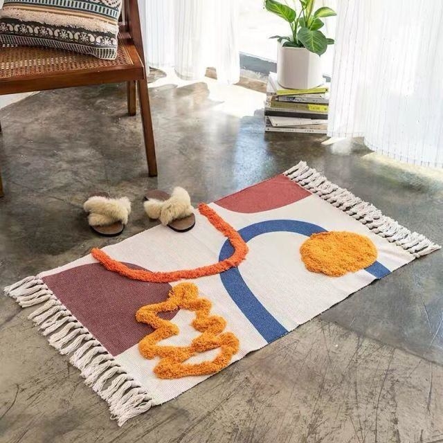 an abstract rug with orange blue and maroon shapes on an oatmeal colored background