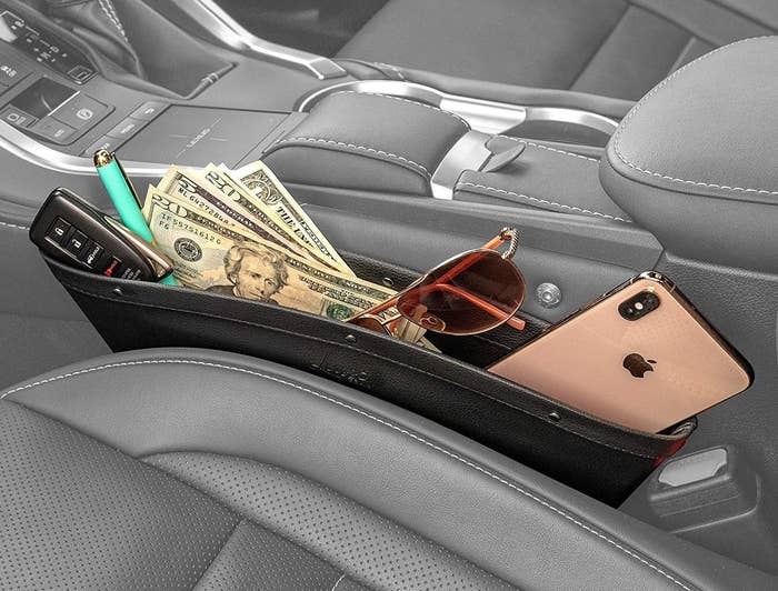 a pocket filled with a phone, sunglasses, money, and keys, tucked into the crevice between the driver&#x27;s seat and center console