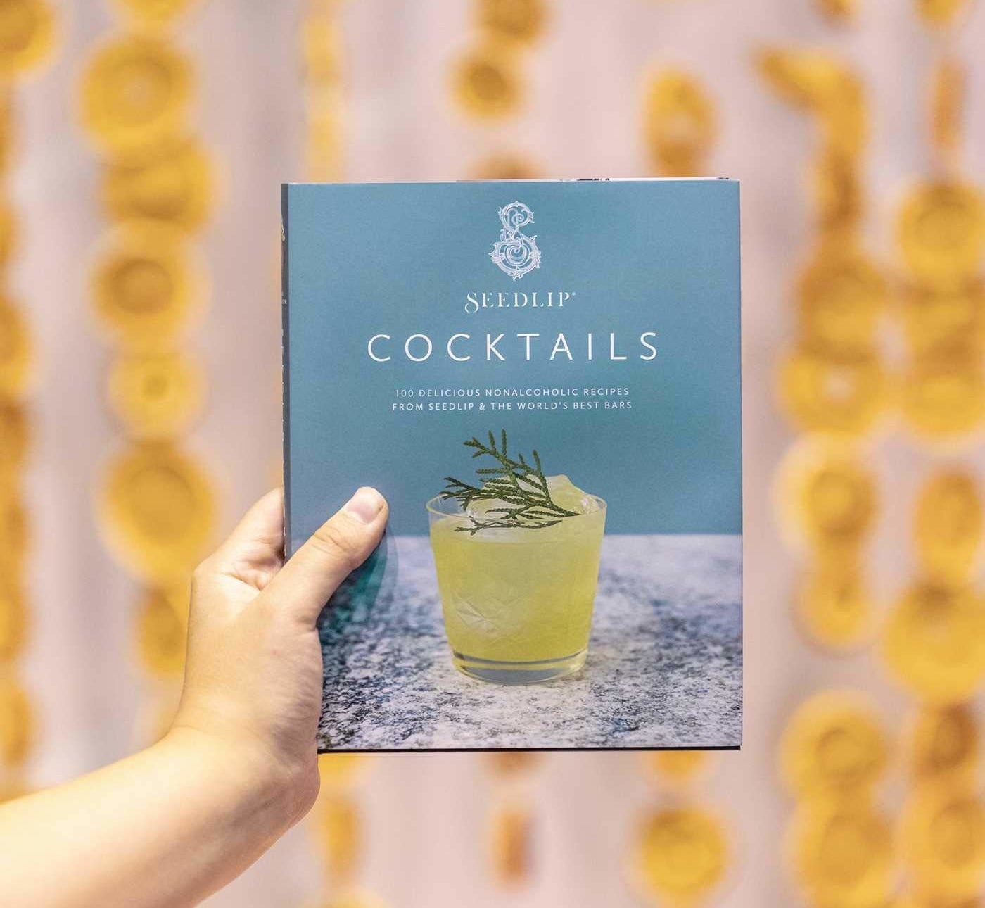 A person holding up a book titled seedlip cocktails