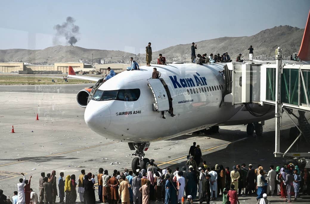 Afghan people climb atop a plane as they wait at the airport in Kabul