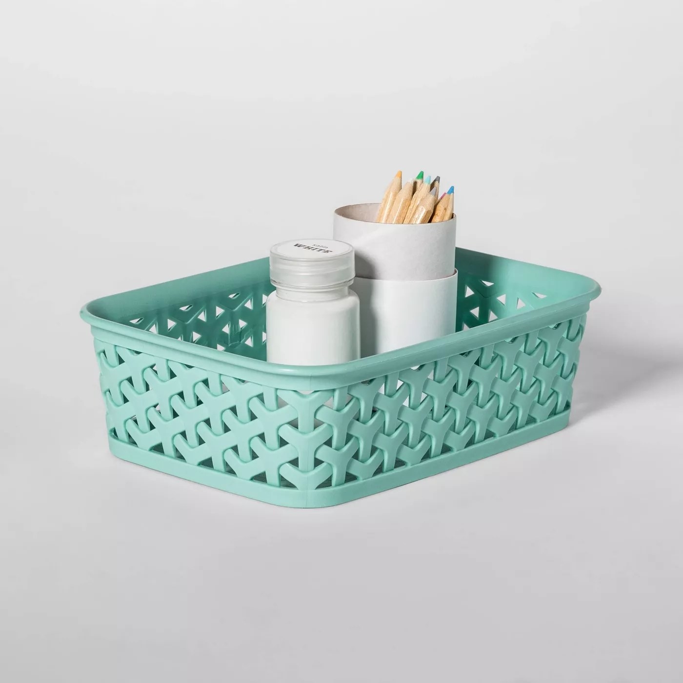 The basket is a jade/teal color and is holding two white containers with colored pencils inside one of them