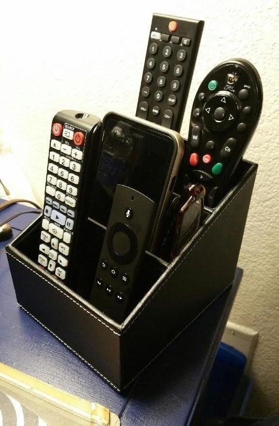 reviewers remote organizer with four remotes, a phone, and glasses inside