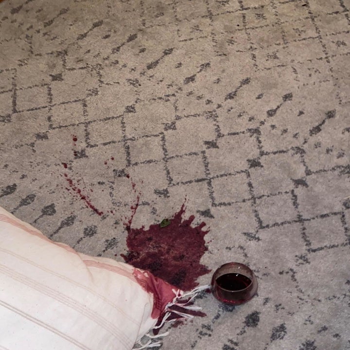 reviewer showing a rug with a big red wine spill on it