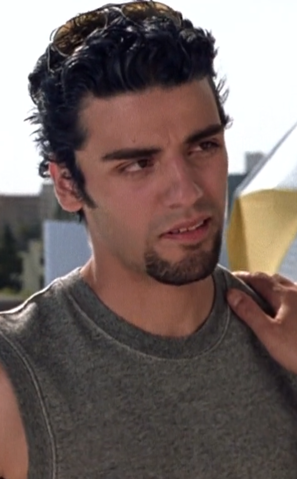 Oscar Isaac with a goatee beard, wearing a tank top and sunglasses on top of his head