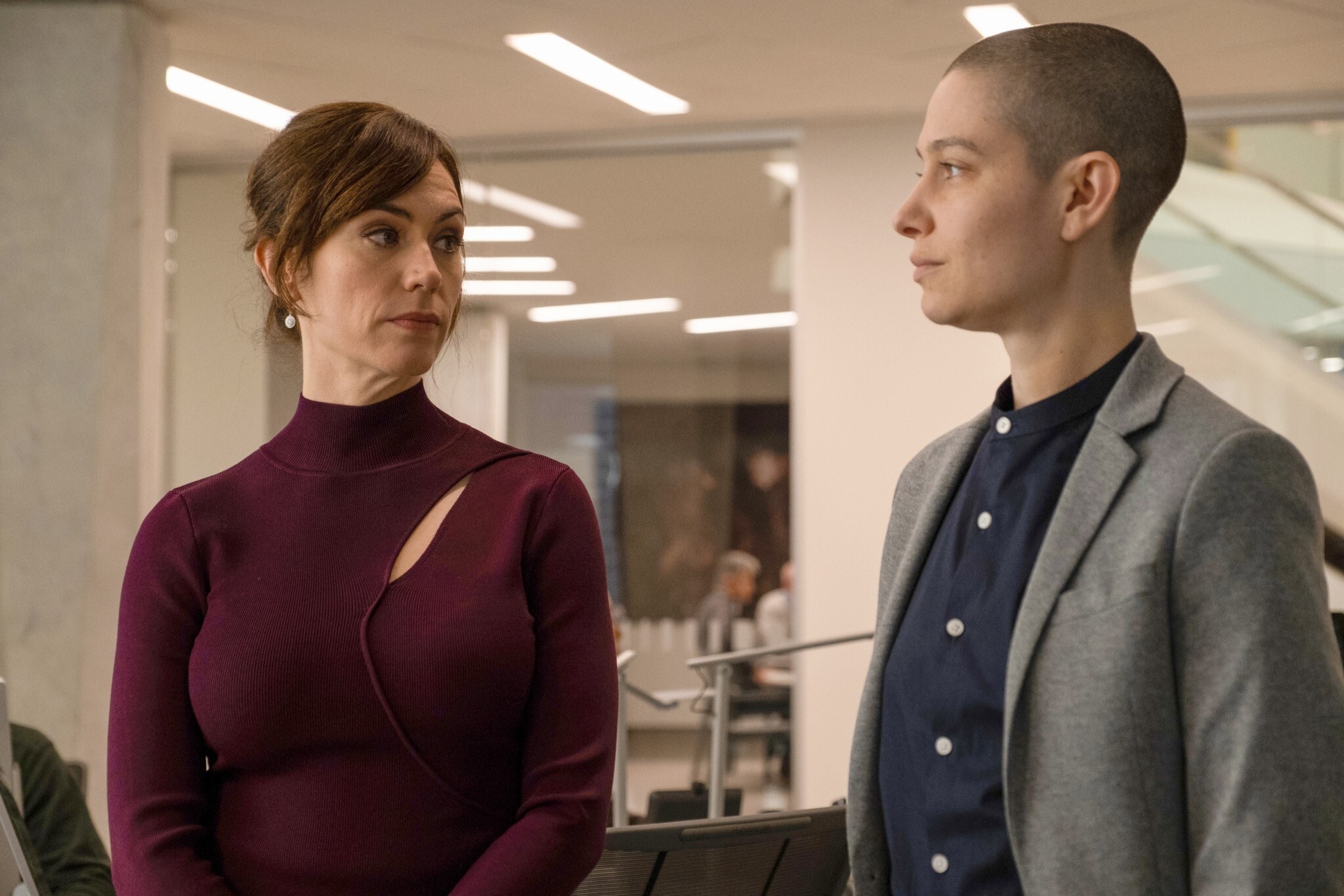 Maggie Siff and Asia Kate Dillon look at each other in an office