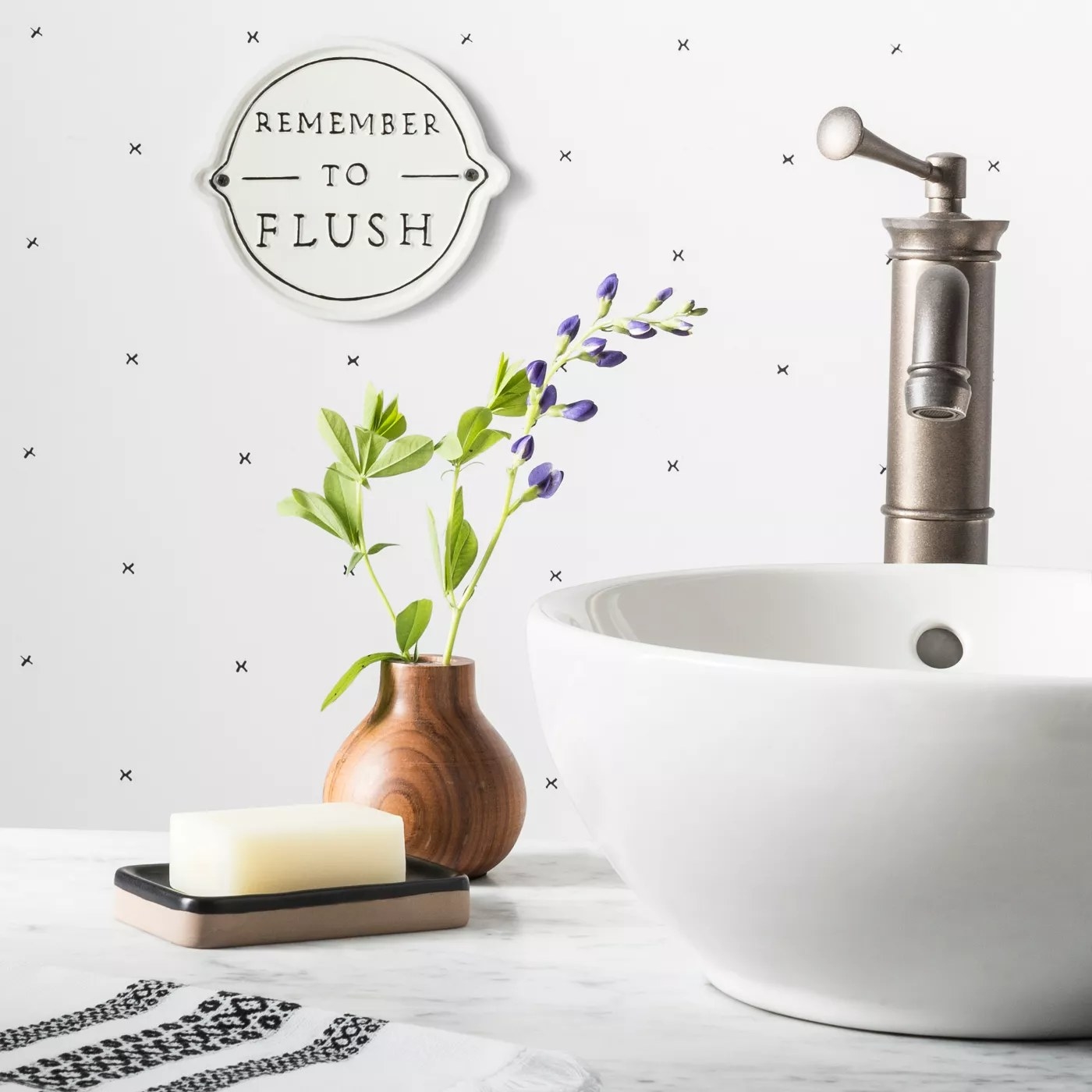 The white lemon-shaped sign says &quot;REMEMBER TO FLUSH&quot; in black serif font and is hung in a white bathroom with small pops of color from plants, decor and supplies