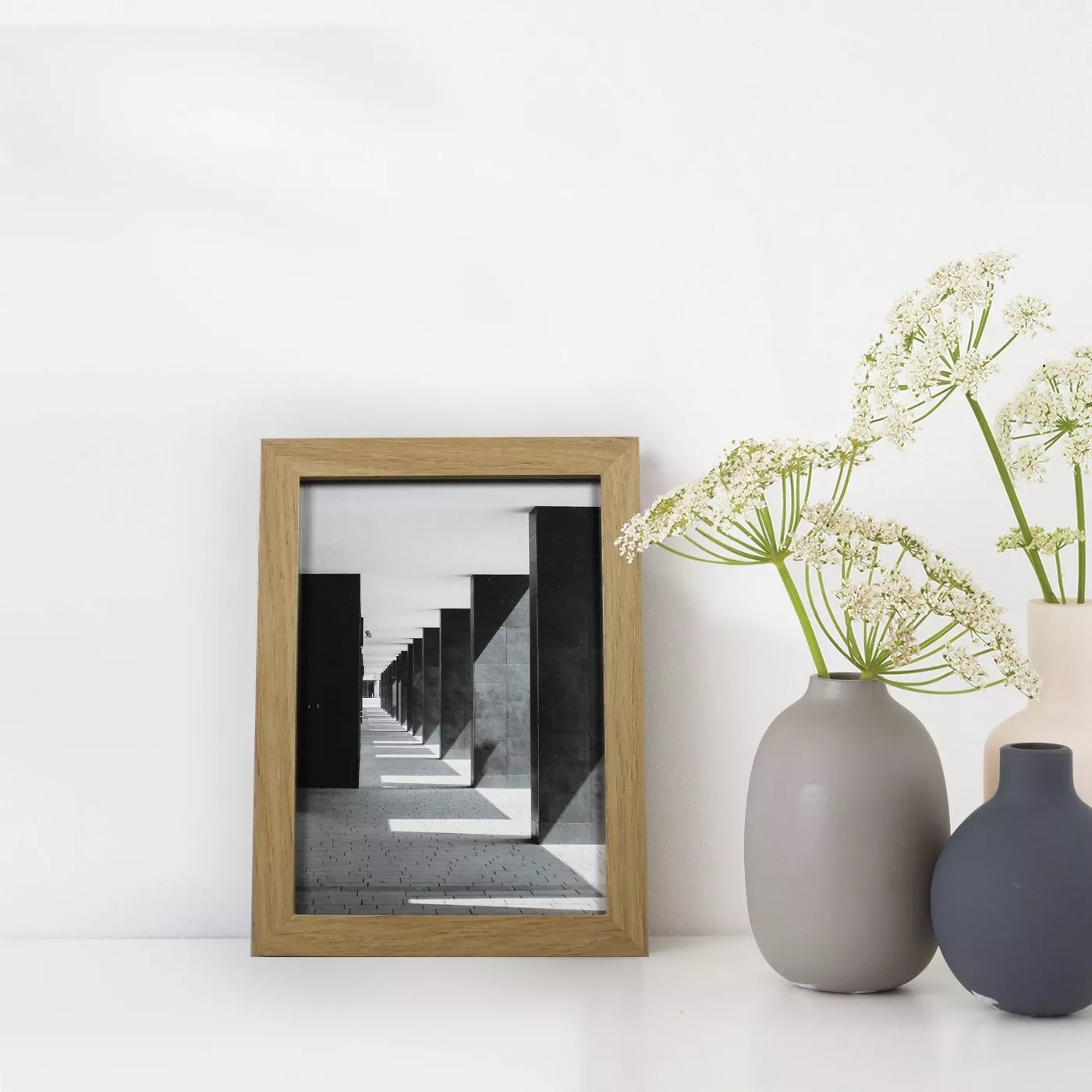 The light brown frame has a black and white stock architecture photo and is next to pastel colored pottery holding flowers