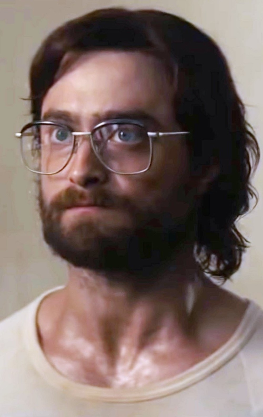 Daniel Radcliffe with long hair, a beard, oversized glasses, while sweating in a shirt