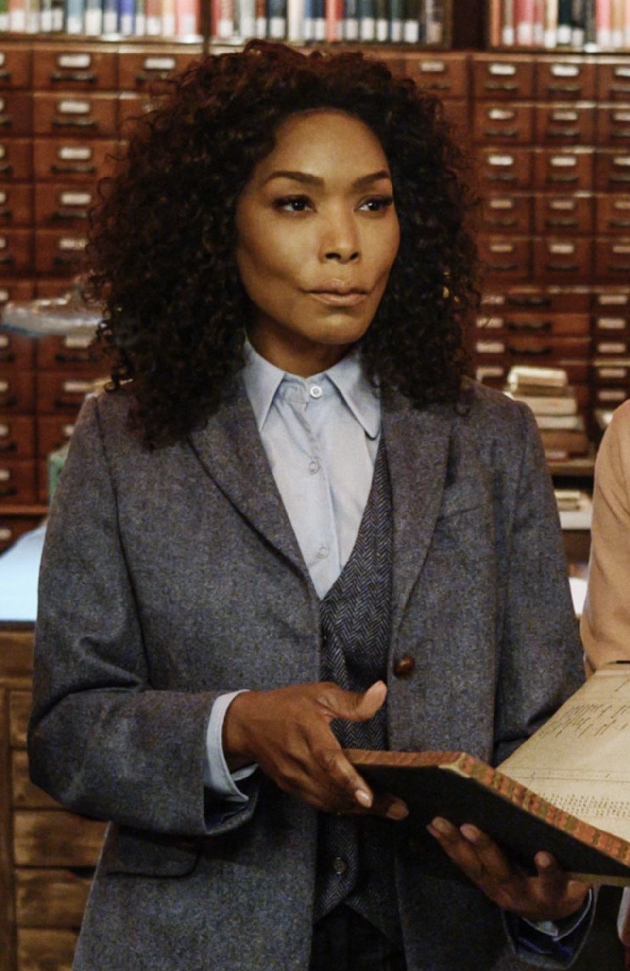 Angela Bassett wearing a three-piece suit while holding a book