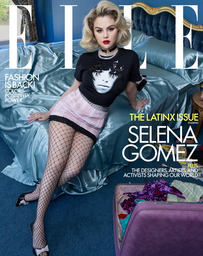 Selena sitting on a bed with satin sheets while wearing a t-shirt, fishnet stockings and heels on the cover of Elle