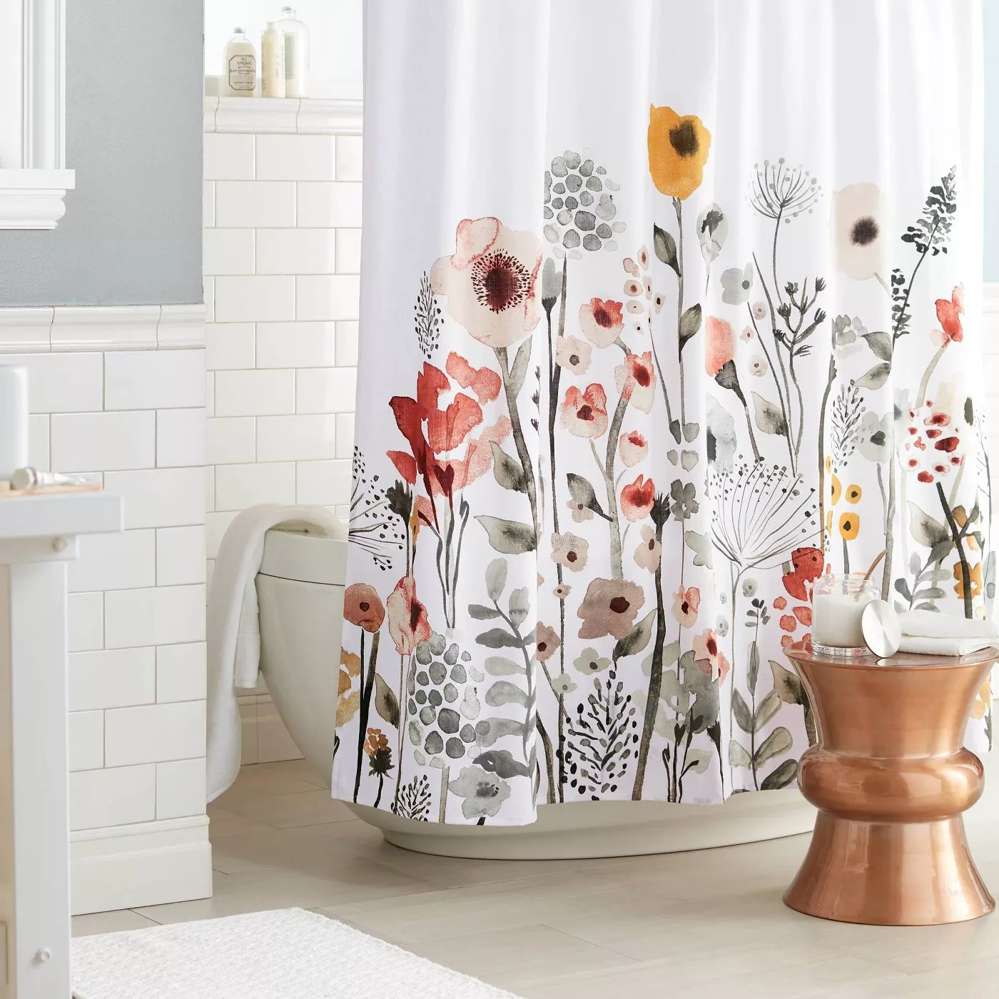 The white shower curtain has a bright watercolor floral pattern climbing up from the bottom