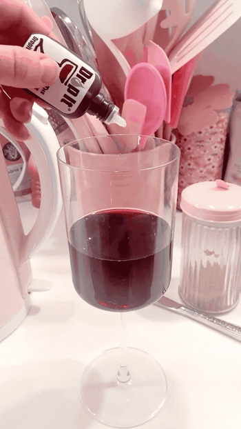 BuzzFeed editor adding two drops to a glass of red wine