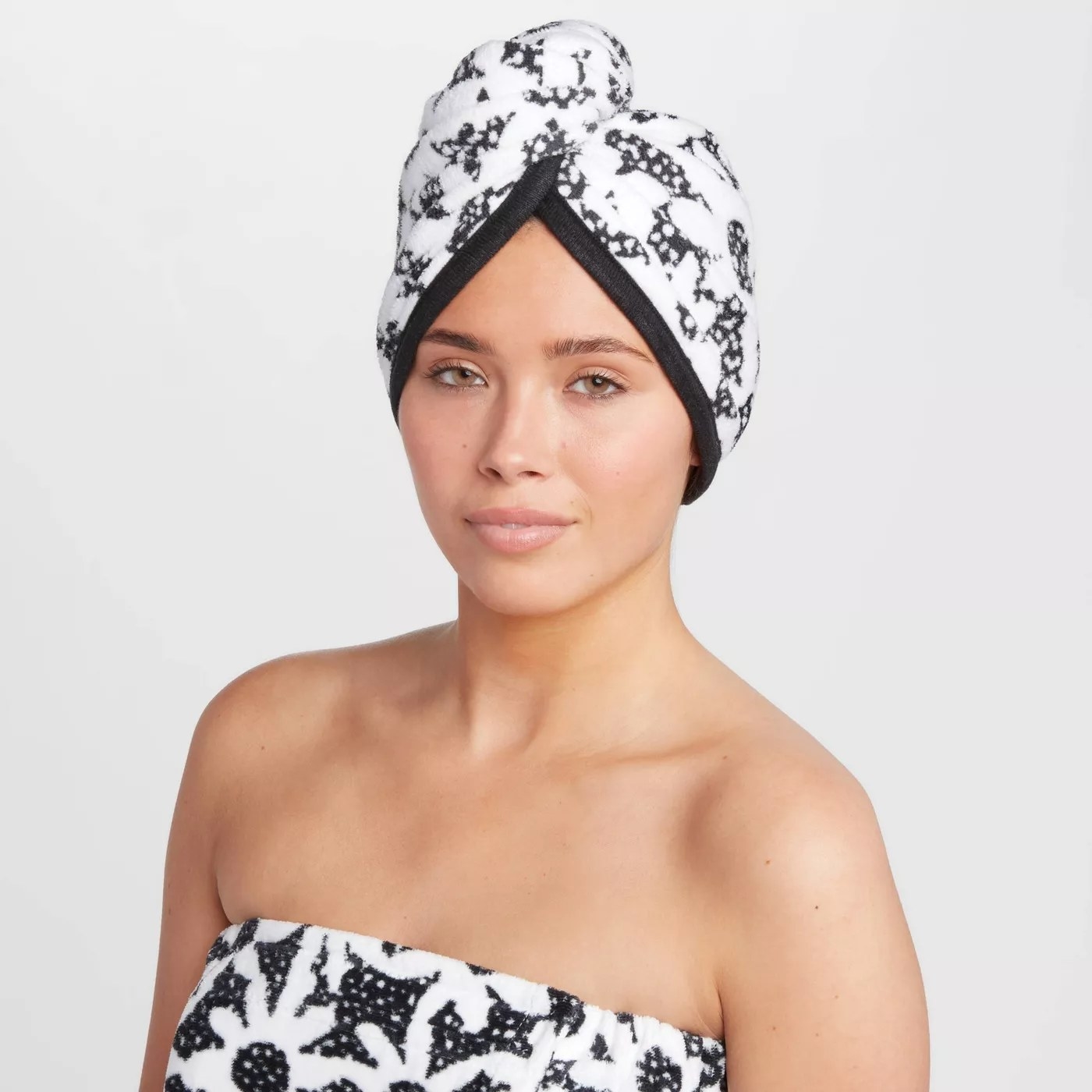 An adult is wearing their hair wrapped in a black and white floral hair wrap with a matching body wrap