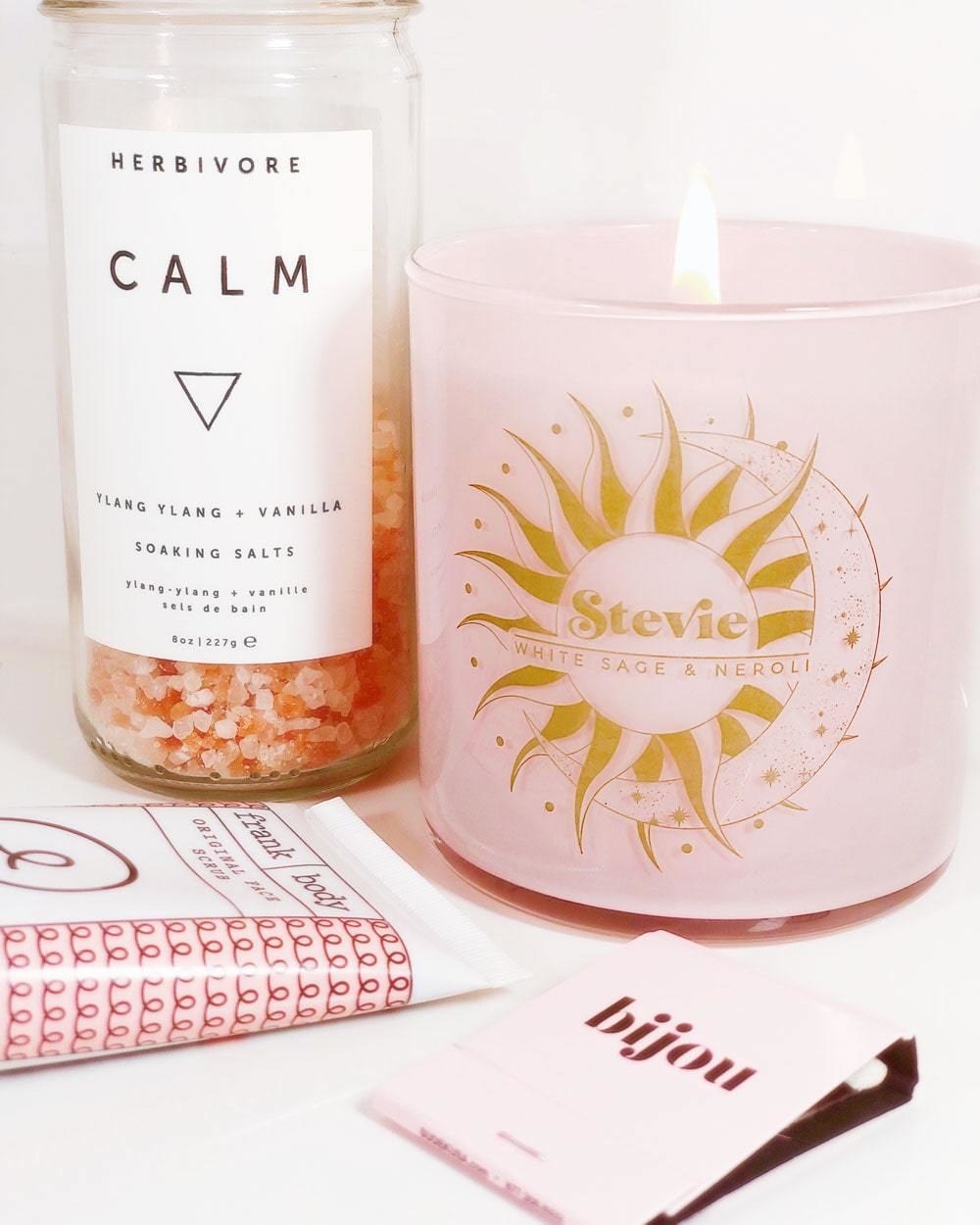 A pink candle with gold sun and moon with the words &quot;Stevie&quot; and &quot;white sage &amp;amp; neroli&quot; on it