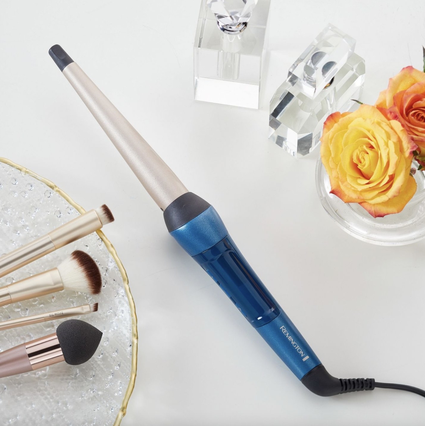A hair curling wand with makeup brushes and a rose