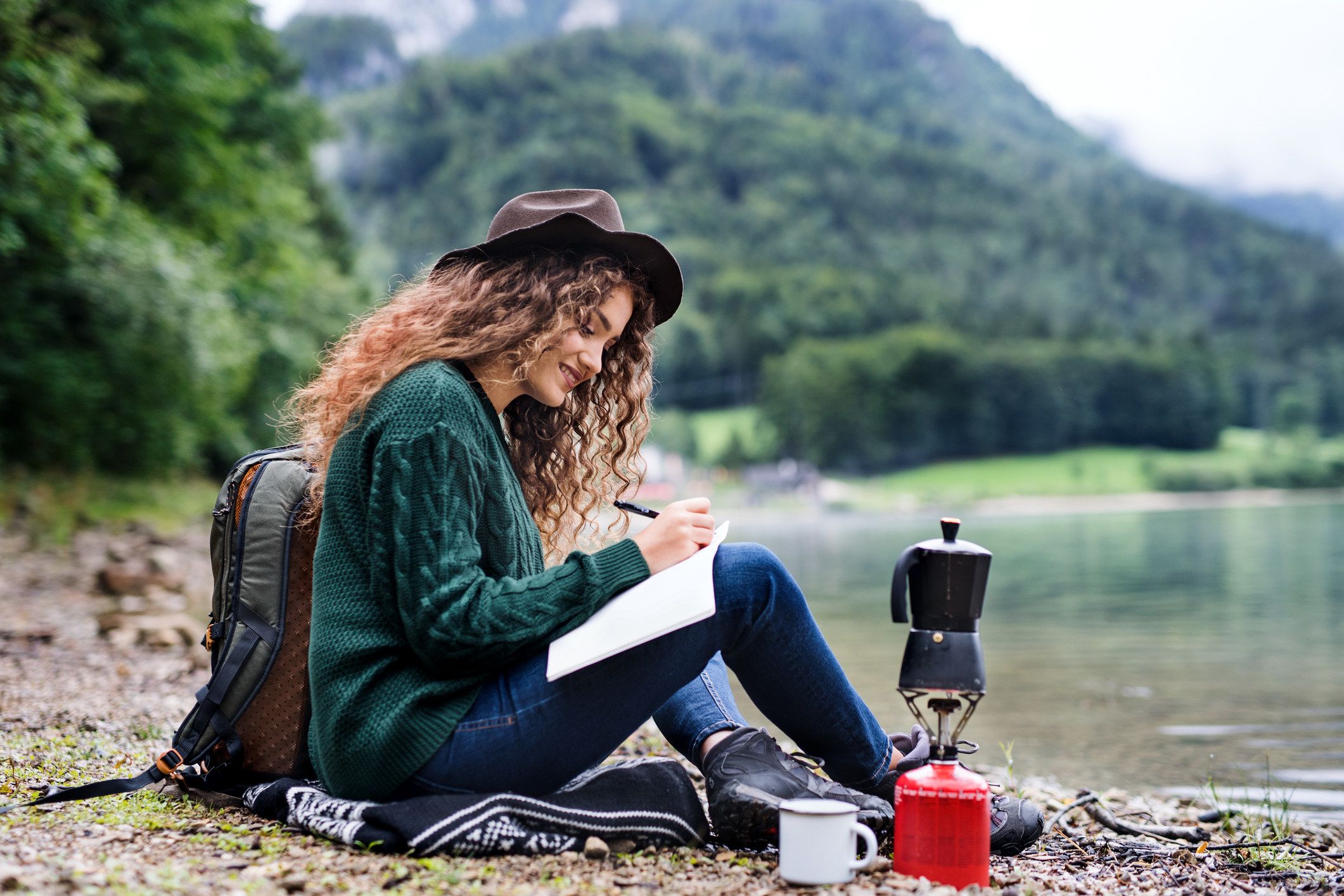 Woman writing while sitting by a creek and some mountains