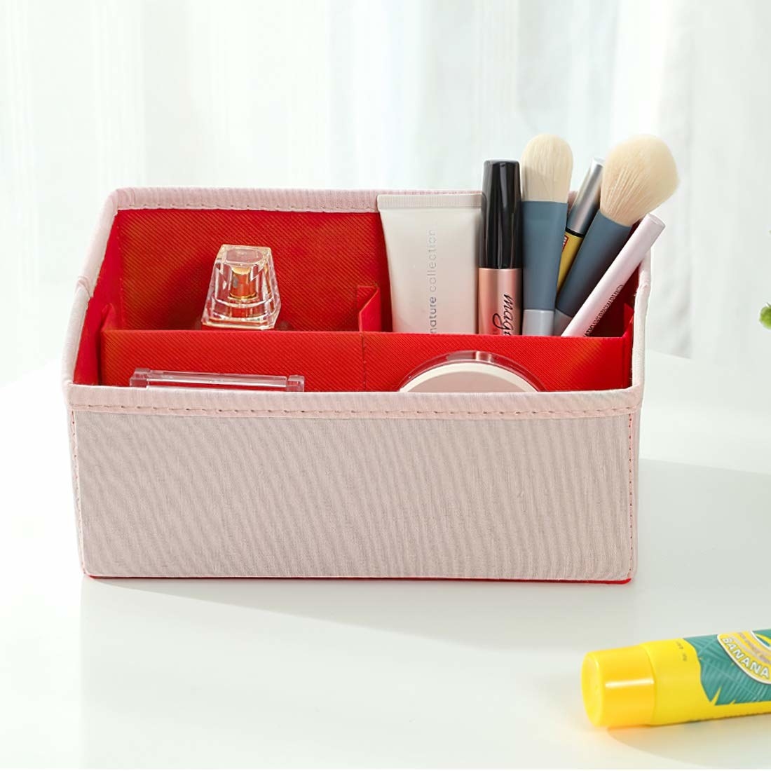 An organiser box that is pink on the outside and red on the inside containing cosmetics