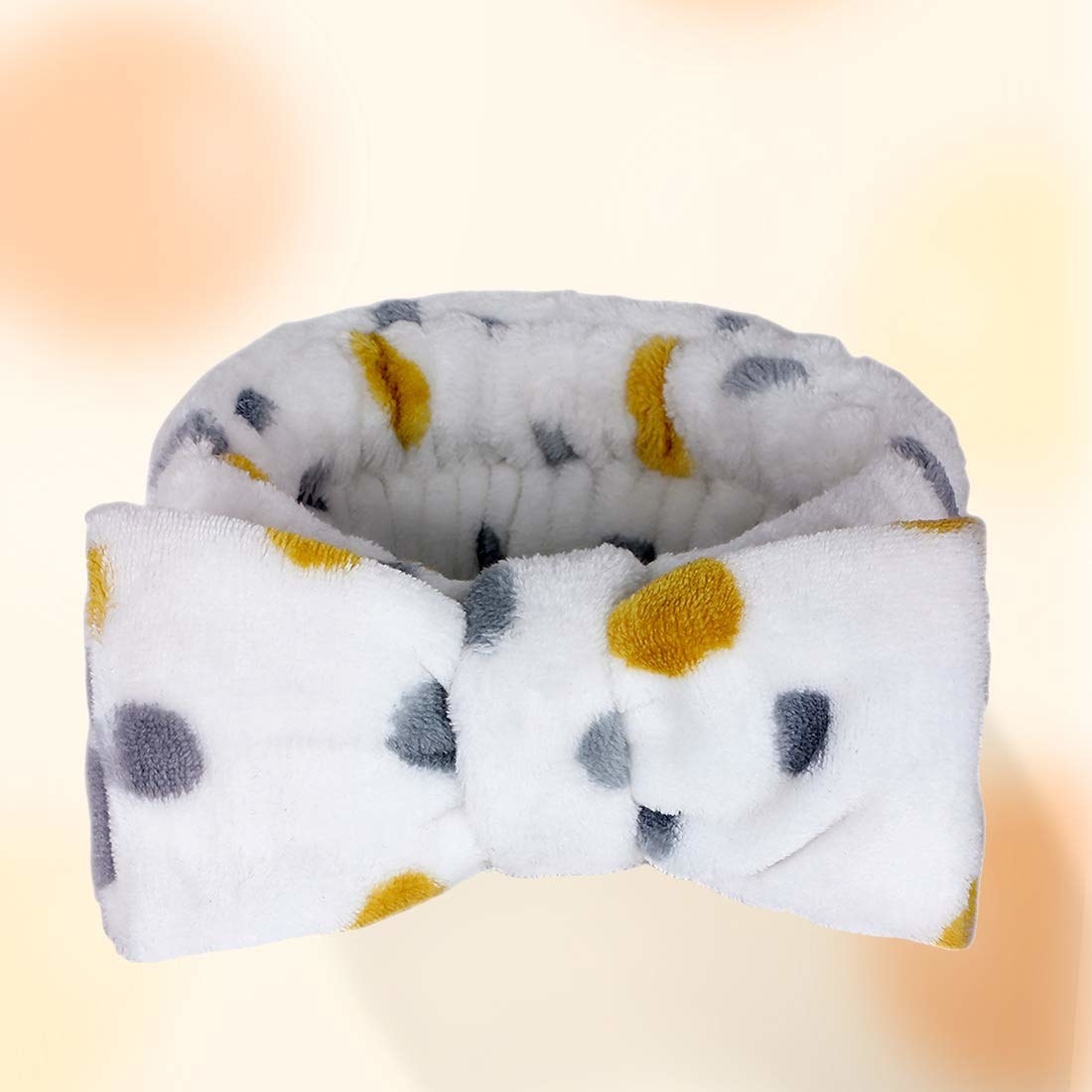 A white hair wrap band with a bow and yellow and grey polka dots on it