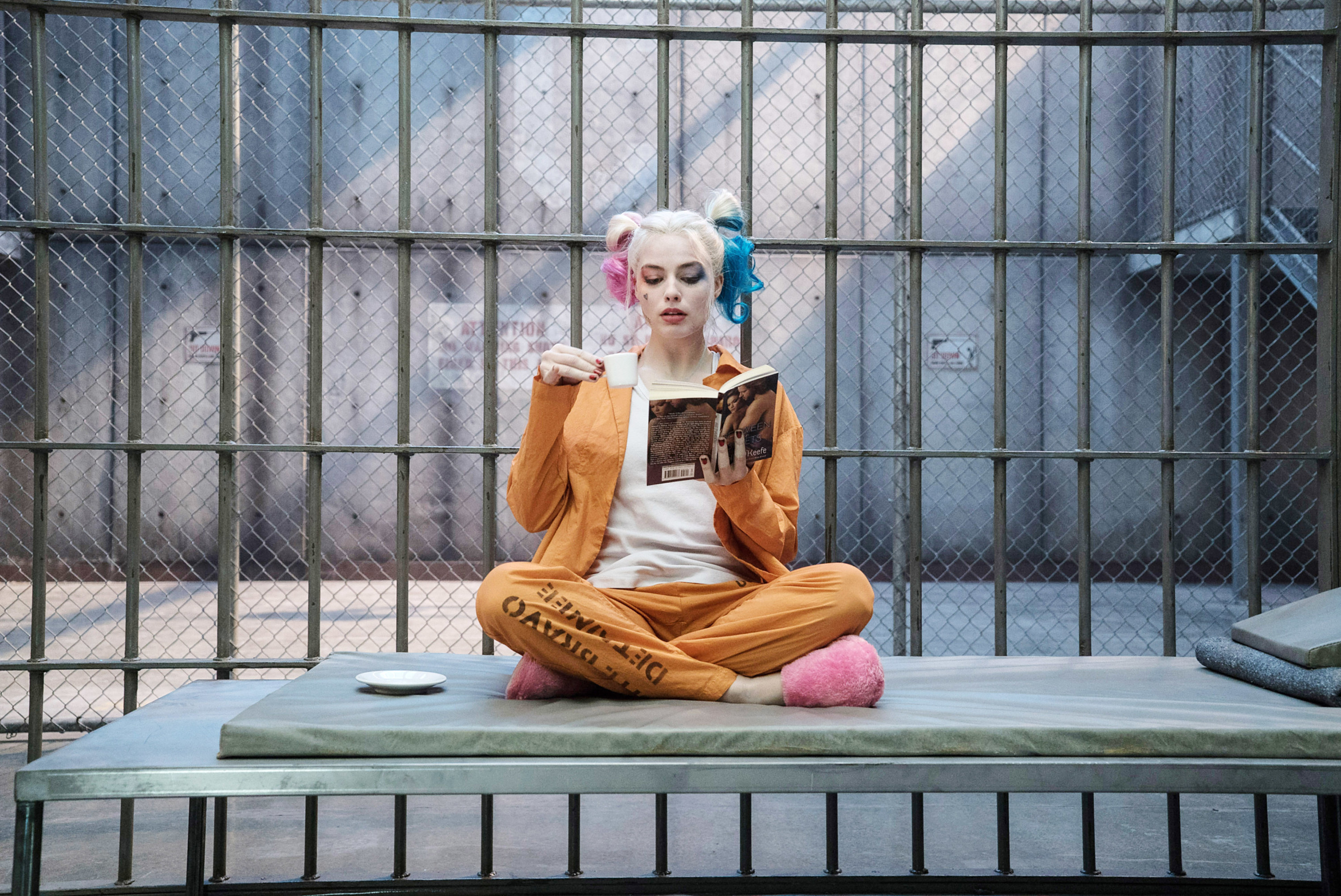 Harley in prison scrubs with the shirt open and a plain shirt underneath, and fuzzy slippers, with bun pigtails