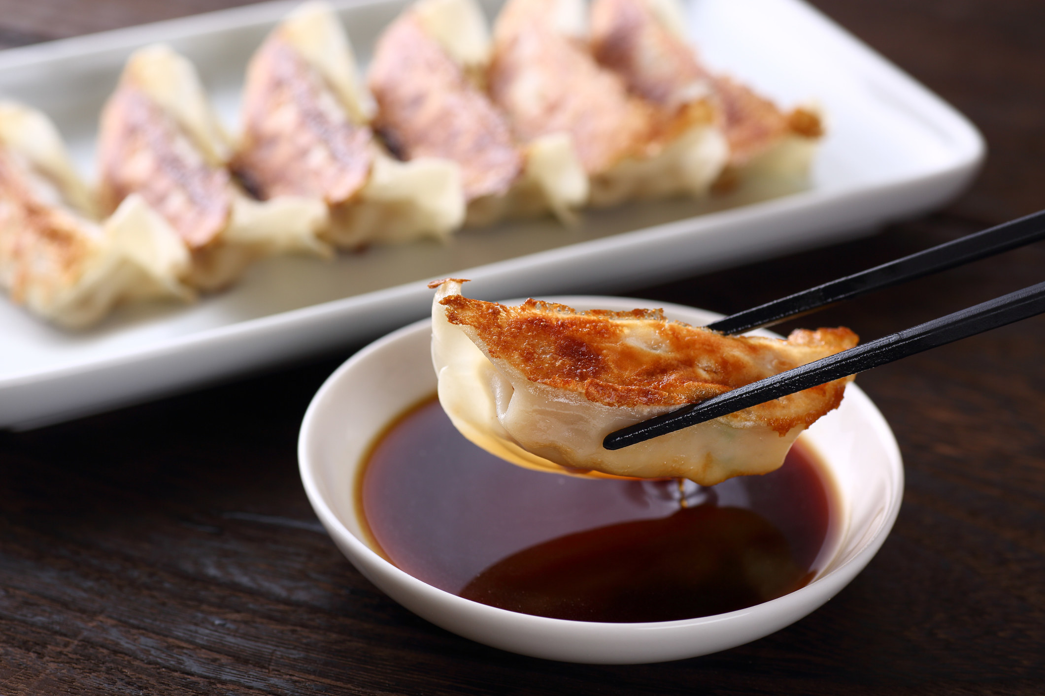 Someone dipping a gyoza into soy sauce.