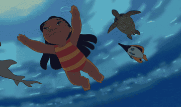 An upwards angle shot of Lilo as she swims under the surface of the ocean with a shark and various fish