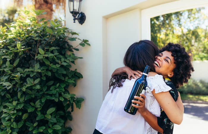 Two friends greet each other with a hug. One woman holds a gifted bottle of wine.