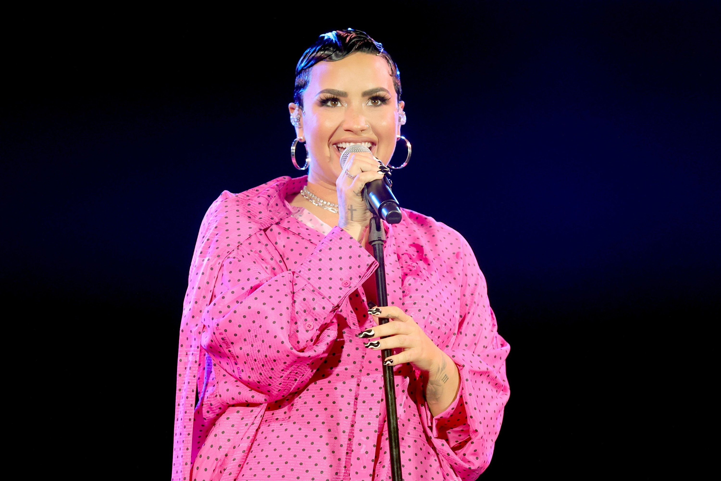 Demi smiles on stage while wearing a pink polka dot oversize shirt