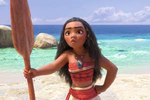 Moana standing in front of the ocean with an oar in her hand and a hand on her hip