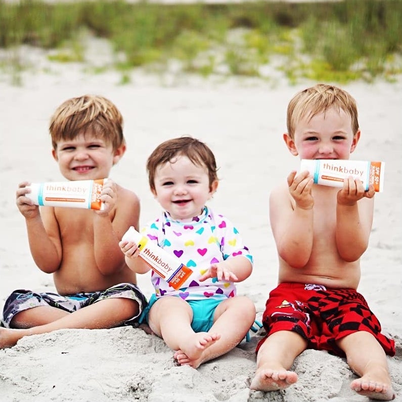 Three kids holding the tubes of sunscreen on the beach