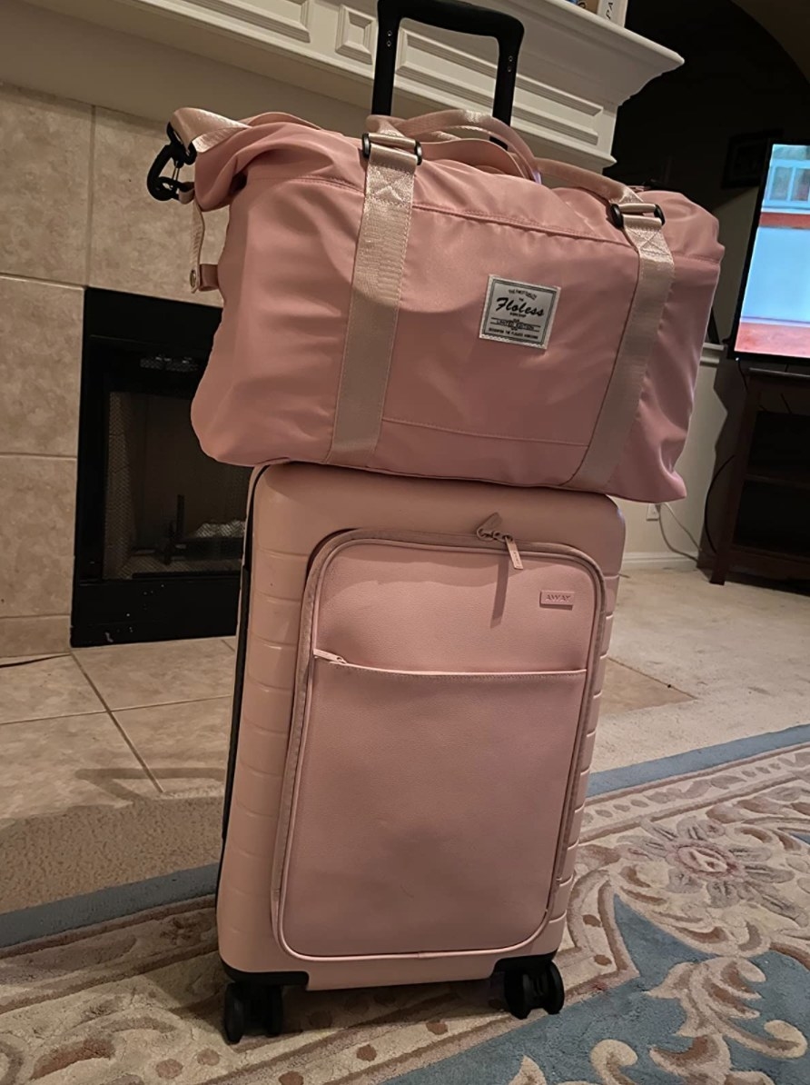 the reviewer&#x27;s photo of the duffle bag in pink on top of a carry on suitcase