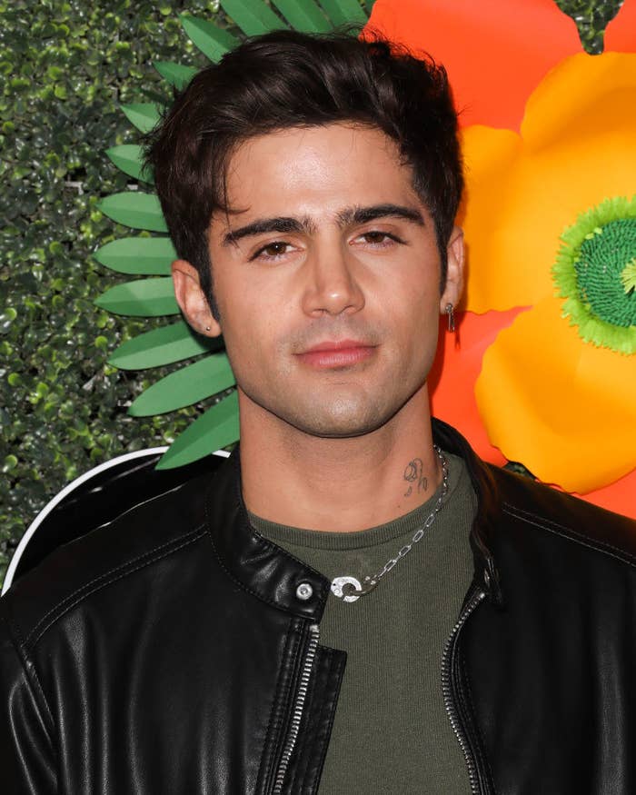 Max Ehrich posing on a red carpet in a T-shirt and leather jacket