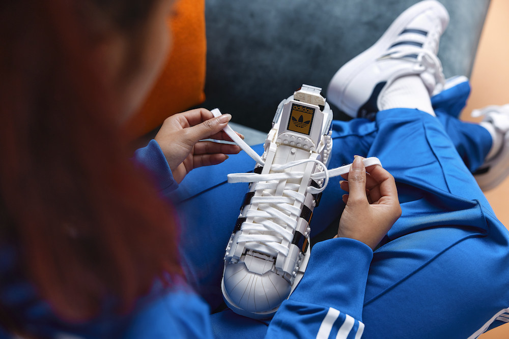 A person holding a LEGO Adidas show in the lap and tying the shoelaces