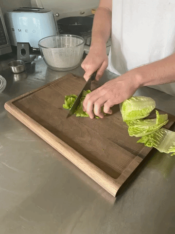 gif of the writer&#x27;s walnut cutting board on a stainless steel counter top being used to slice lettuce