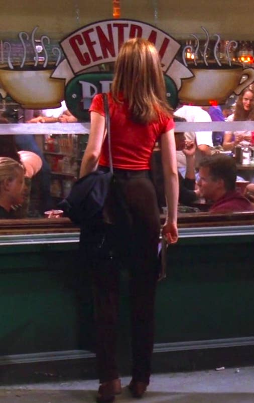 Rachel wearing slim pants, a red shirt, and a cute off-the-shoulder bag, but also weird sandal heels