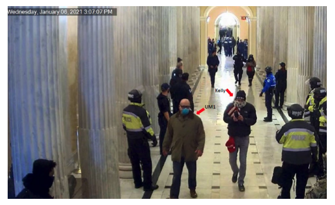 A number of people, including several wearing police uniforms, stand and walk along a hallway