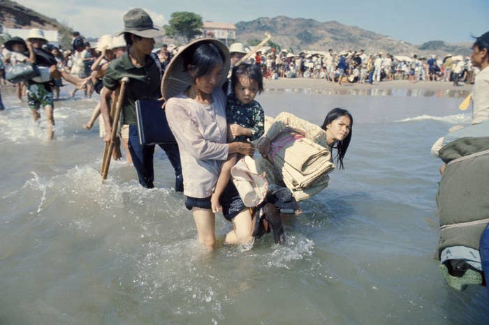 A woman in the foreground carrying a child wades through water