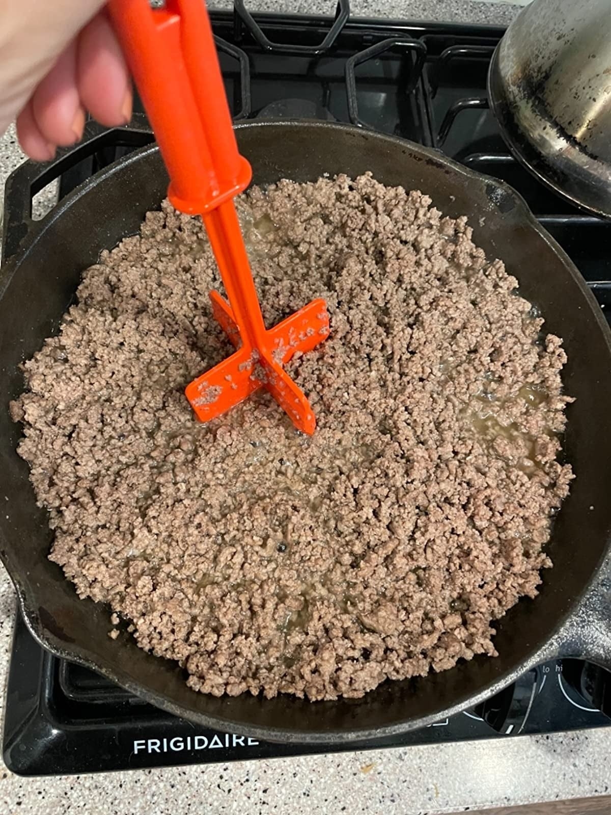 a reviewer chopping meat in a pan with a red chopper tool