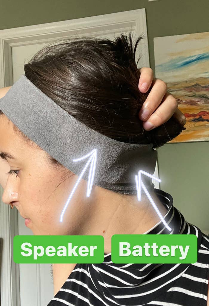 writer wearing the grey fleece circular headband with arrows pointing to the hidden speaker over her ear and the hidden battery pack at her neck