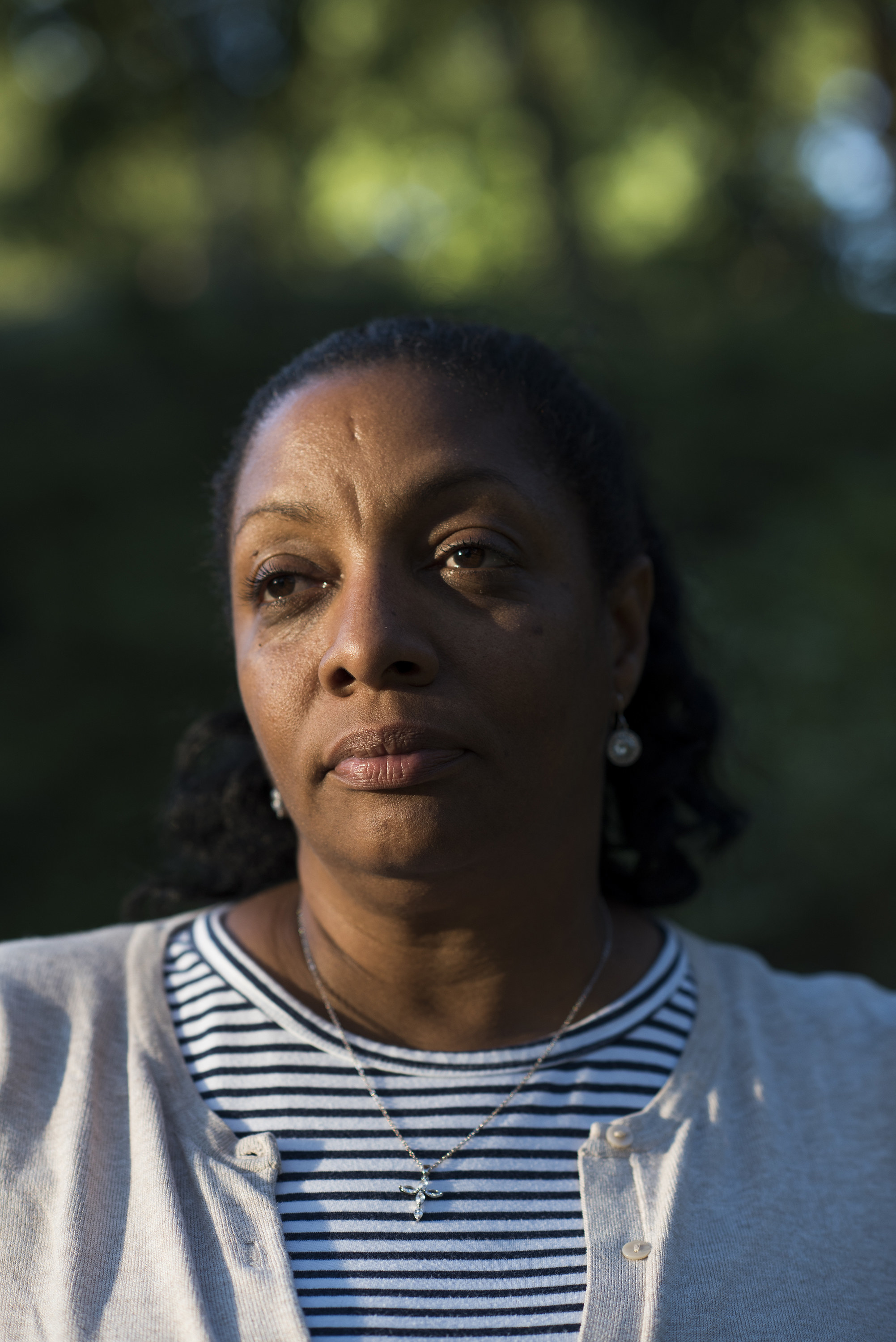 A woman with a striped shirt and a cross stares past the camea