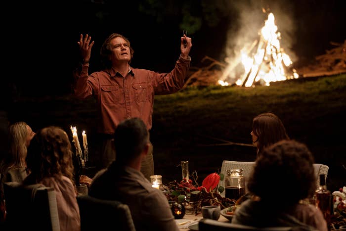 Michael Shannon standing  with his arms raised and looking up in front of a group around a table