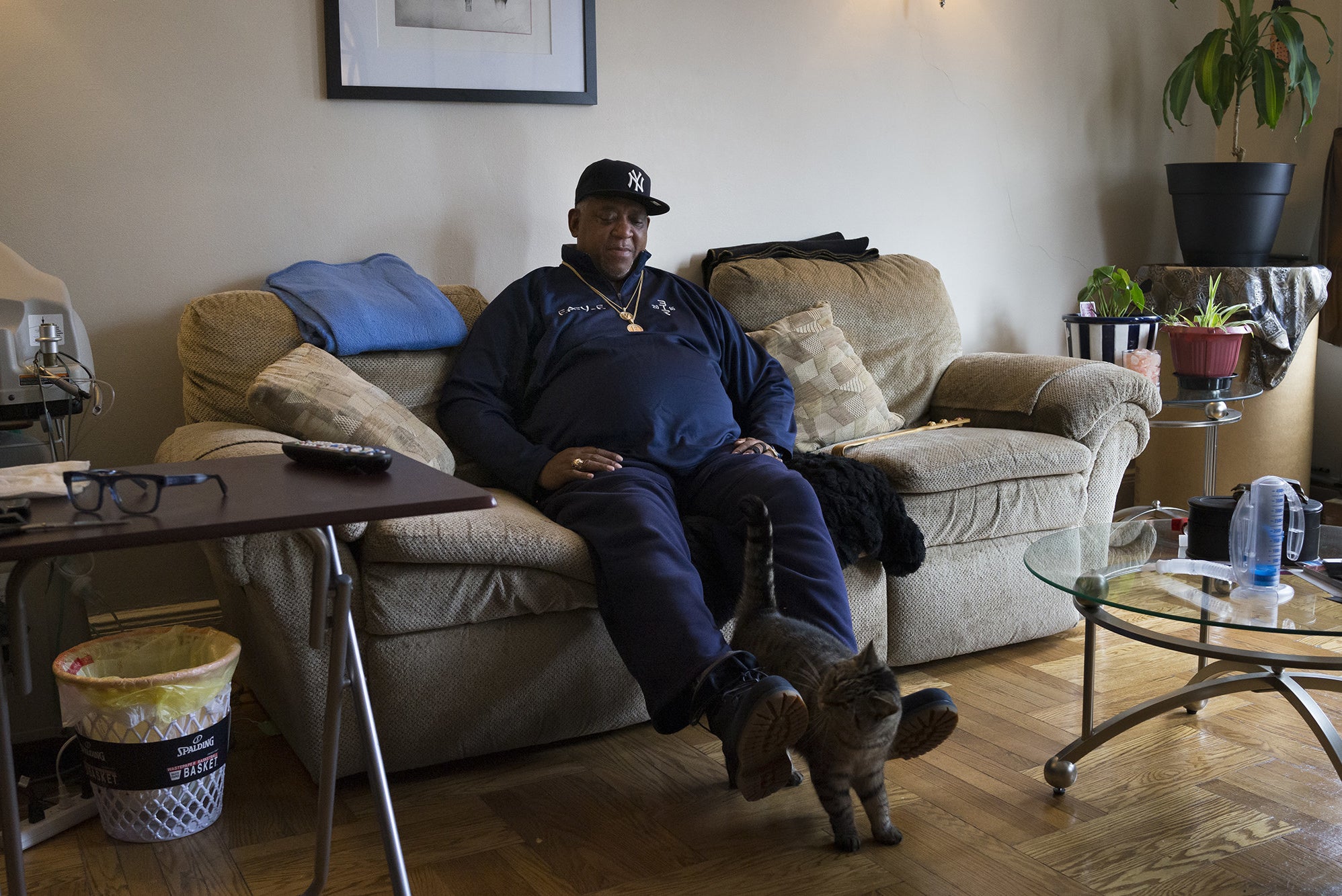 A man sits at home on his couch with a cat