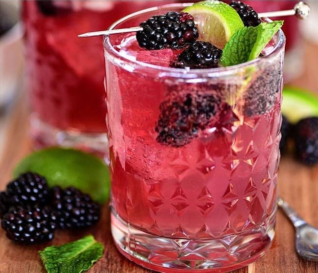 Tumbler full of a red wine, ginger beer, and tequila cocktail, garnished with blackberries and a lime wedge