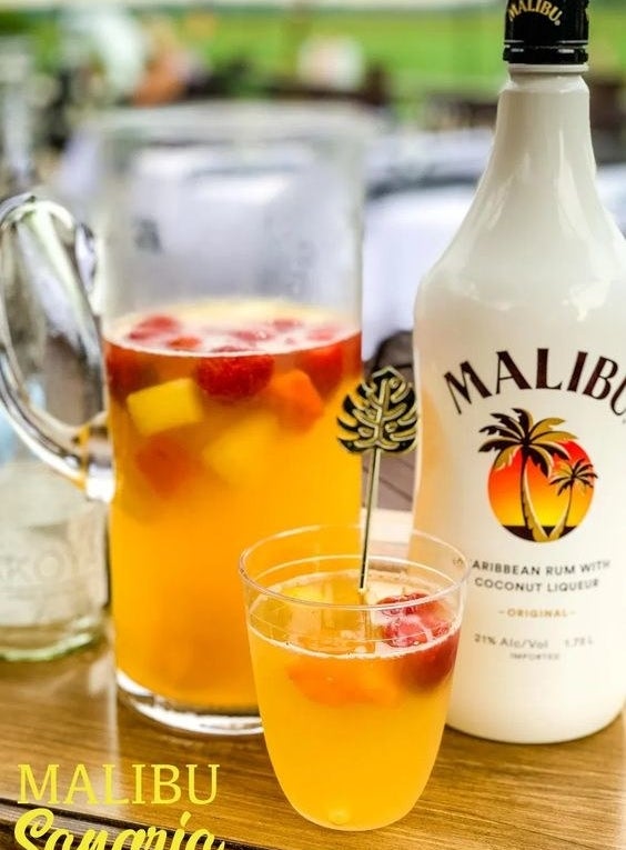 A pitcher of tropical fruit sangria, a glass of the same, and a bottle of Malibu rum.