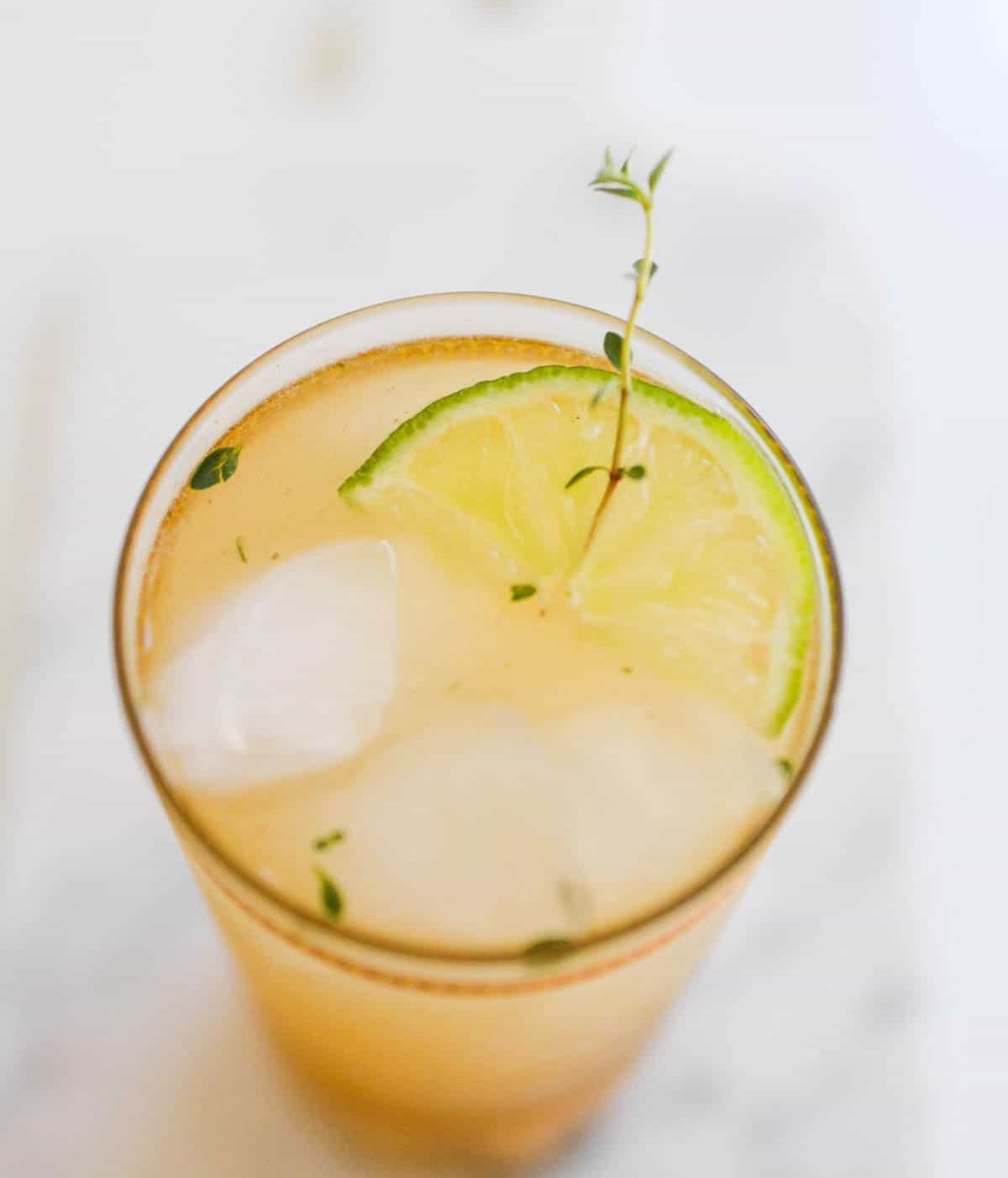 A tall glass of iced chardonnay and pear cocktail, garnished with a thyme sprig