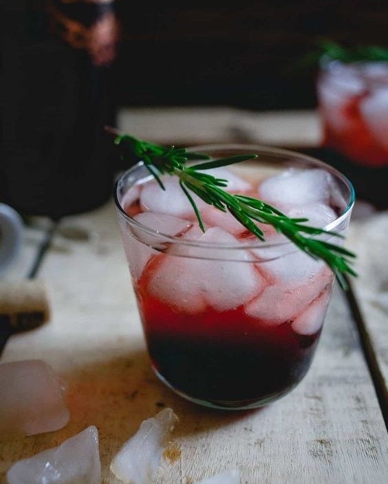 A deep red cocktail of tart cherry juice and red wine, iced and garnished with a rosemary sprig