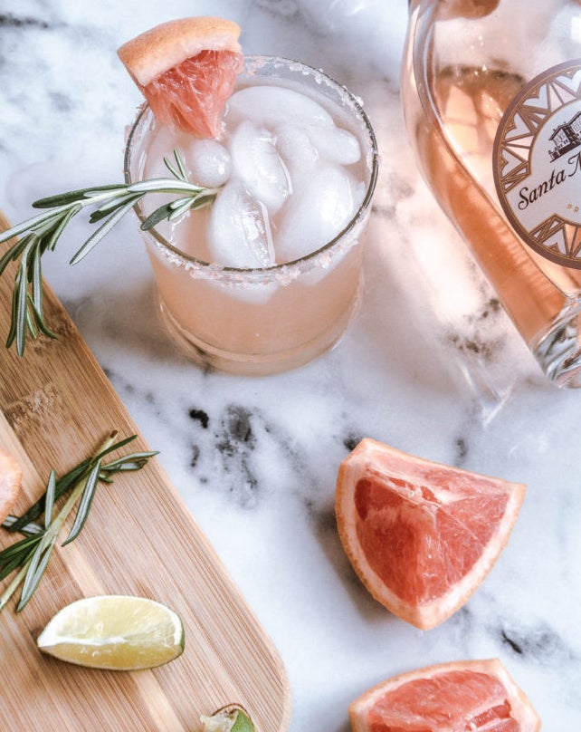 A pale pink margarita made with grapefruit and rosé wine, garnished with grapefruit wedges and rosemary