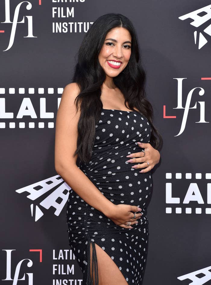 Stephanie cradling her baby bump on the red carpet while wearing a polka dot dress